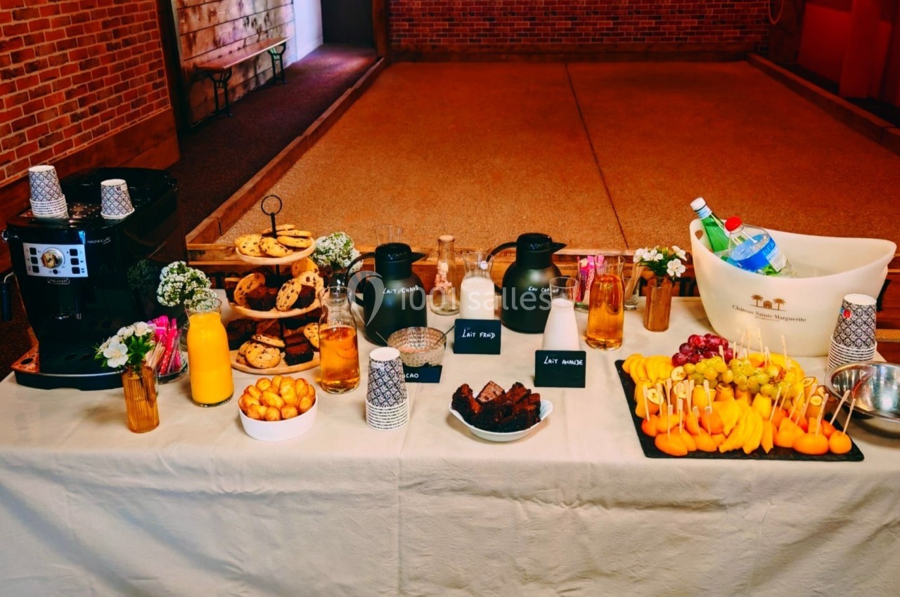 Table dressée avec boissons chaudes, jus, viennoiseries, fruits frais et gâteaux dans un cadre intérieur en briques.