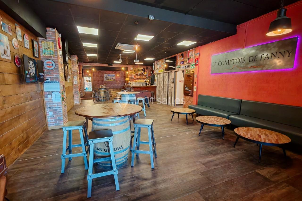 Intérieur d'un bar avec tables en bois, tabourets métalliques, tonneau décoratif et enseigne murale lumineuse.