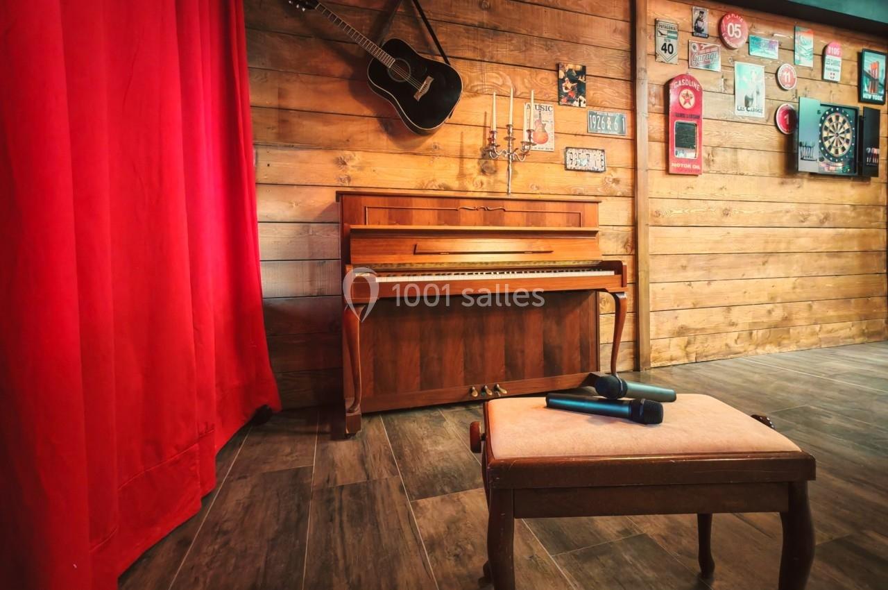 Piano en bois contre un mur décoré de cadres et d'une guitare, avec un tabouret et un micro au premier plan.