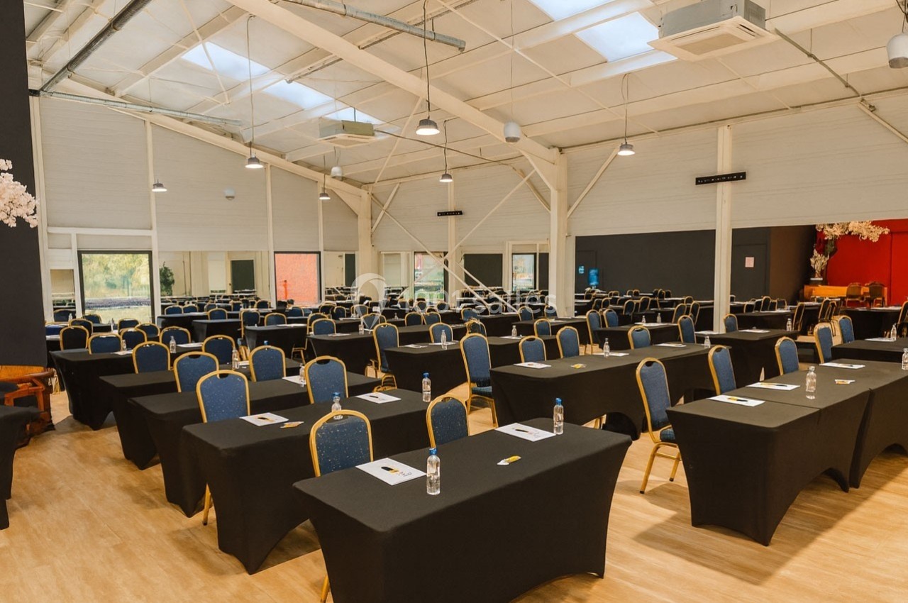 Salle de conférence lumineuse avec des rangées de tables noires et de chaises bleues alignées.