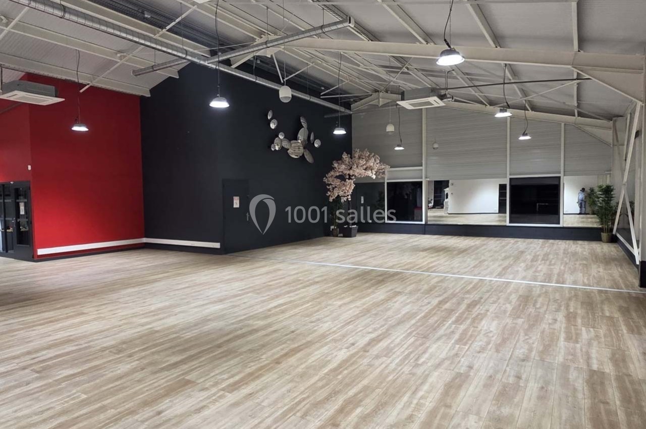 Salle spacieuse avec parquet clair, murs rouges et noirs, éclairage suspendu et décoration murale moderne.