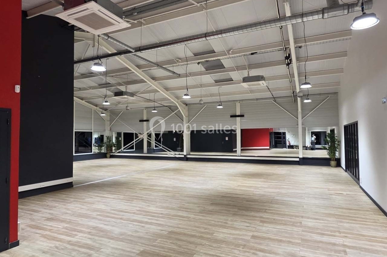 Salle spacieuse avec parquet clair, murs noirs et rouges, miroirs sur un mur, éclairage suspendu et plantes en coin.