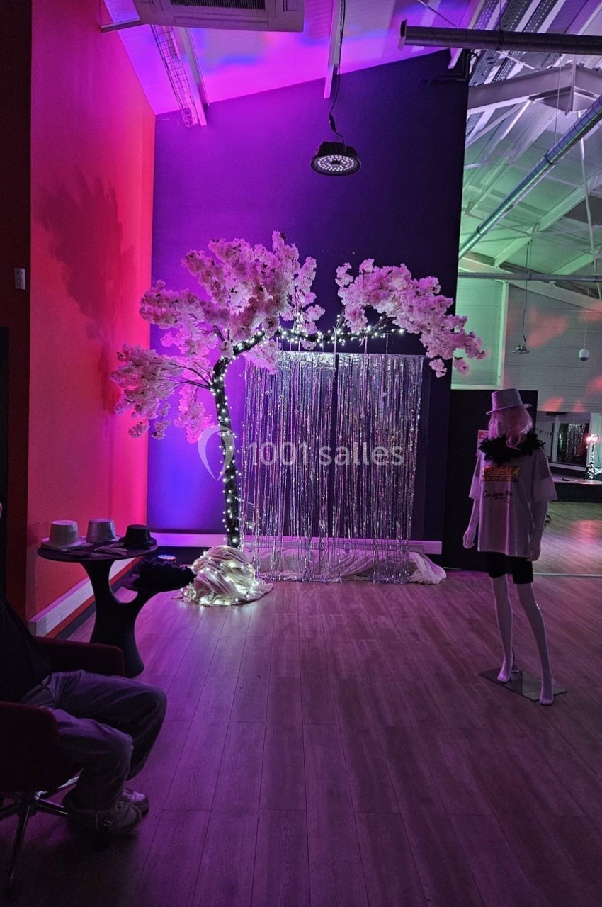 Arbre décoratif éclairé, rideau scintillant et personne debout dans une salle aux lumières colorées.