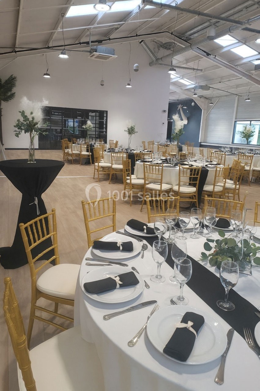 Salle de réception lumineuse avec tables rondes dressées, nappes blanches, chaises dorées et décorations élégantes.