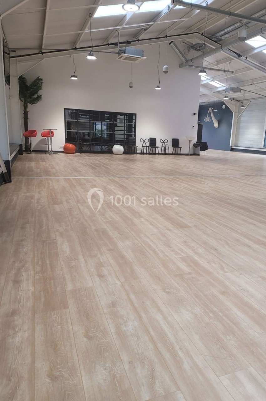 Salle spacieuse avec parquet clair, murs blancs, mobilier minimaliste et grande baie vitrée en arrière-plan.