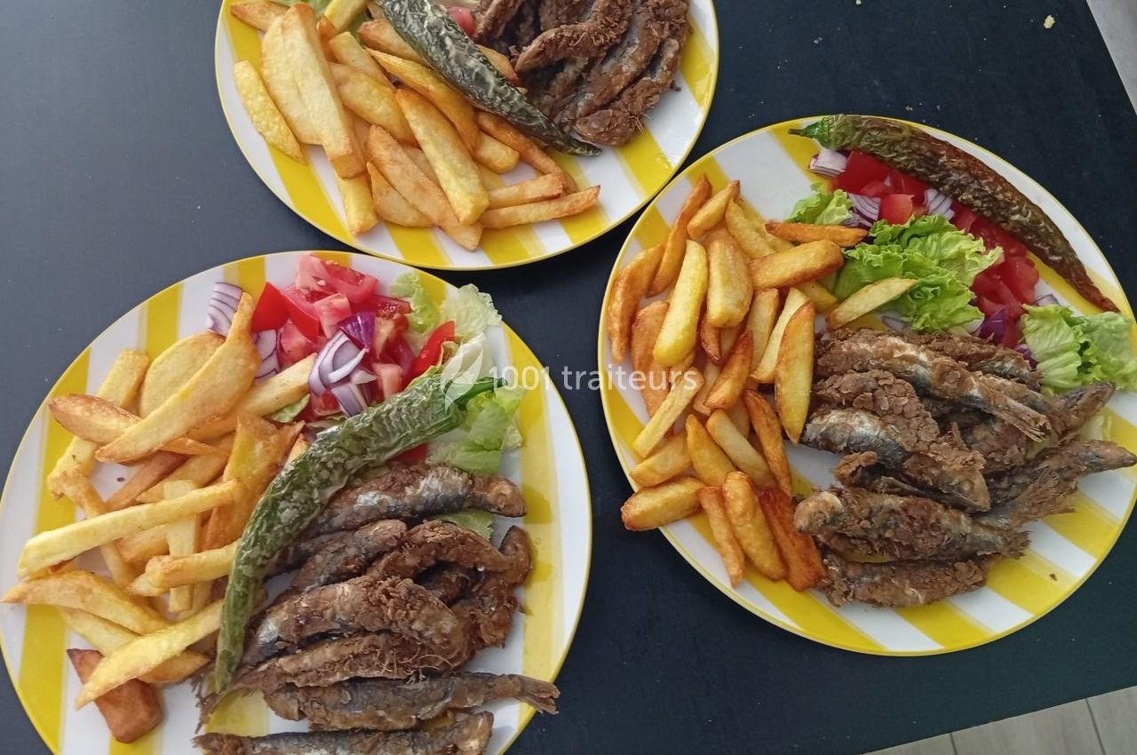 Assiettes contenant des poissons frits, des frites, des légumes frais et un piment grillé sur une table noire.