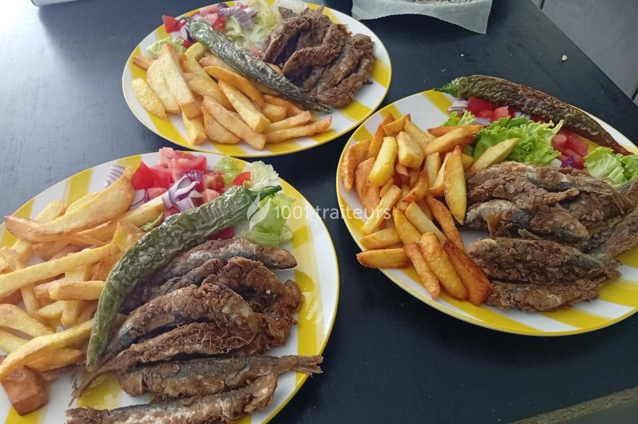 Assiettes composées de frites, poissons frits, salade, tomates, oignons et piments verts sur une table noire.