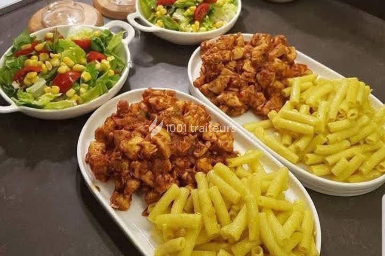 Assiettes de pâtes jaunes accompagnées de poulet en sauce et salades colorées servies dans des bols.