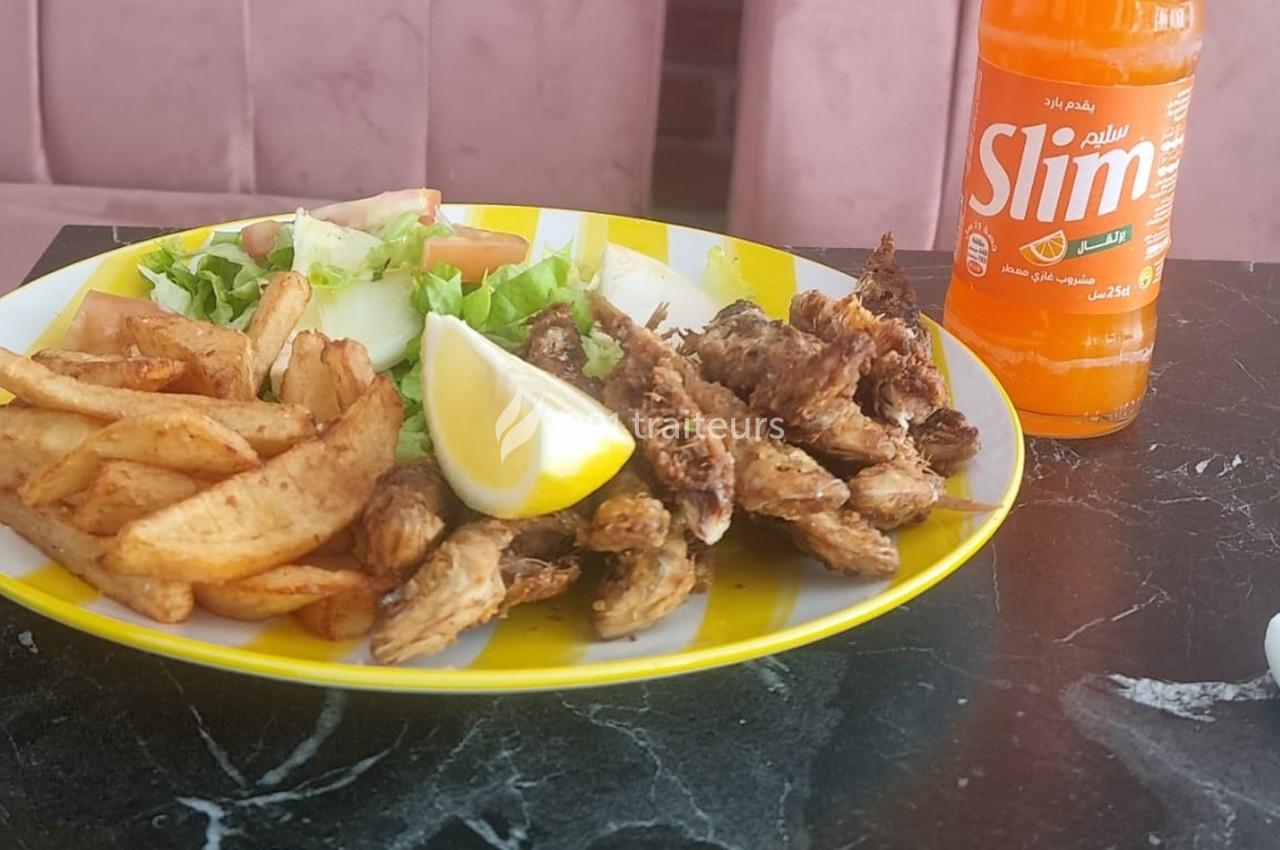 Assiette avec frites, salade, poisson frit et tranche de citron, accompagnée d'une bouteille de boisson orange.