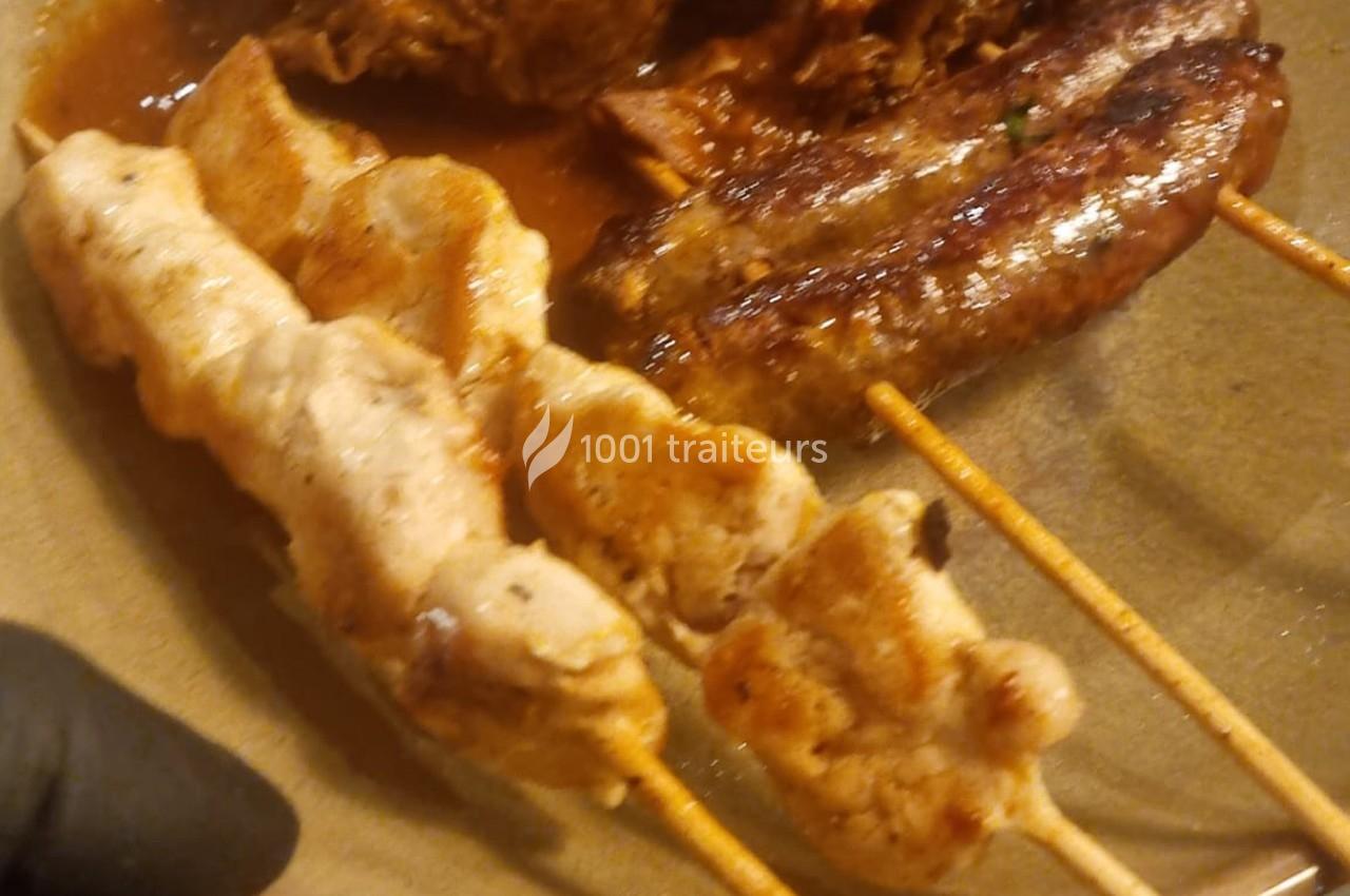 Brochettes de poulet grillé et saucisses servies sur une assiette avec une sauce en arrière-plan.