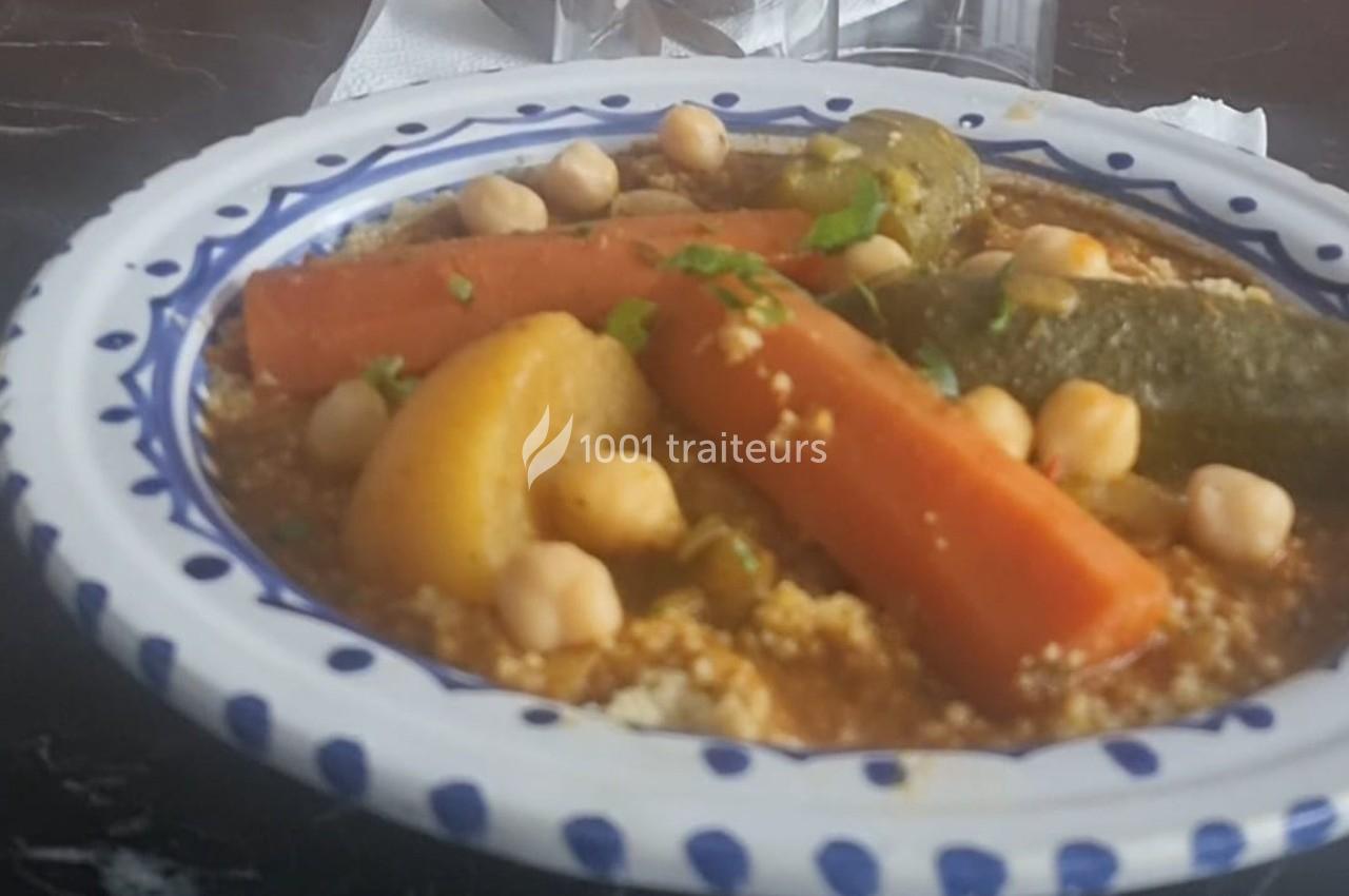 Plat de couscous garni de légumes variés, pois chiches et herbes, servi dans une assiette décorée.