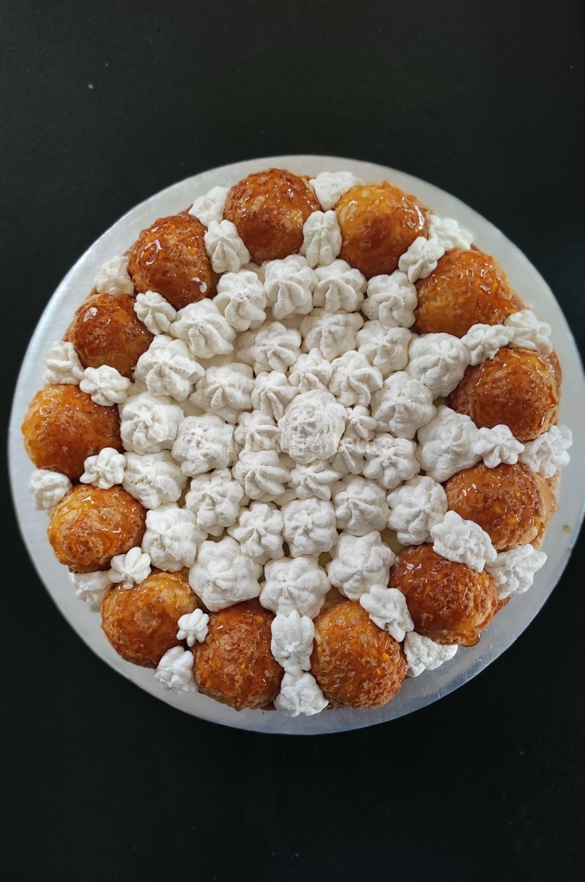 Dessert circulaire composé de choux caramélisés et de crème blanche disposés en motif symétrique.
