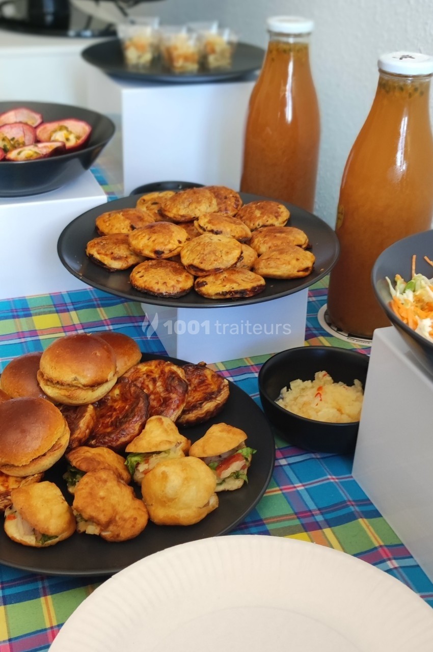 Buffet composé de mini-burgers, bouchées salées, salade de crudités et jus dans des bouteilles en verre.