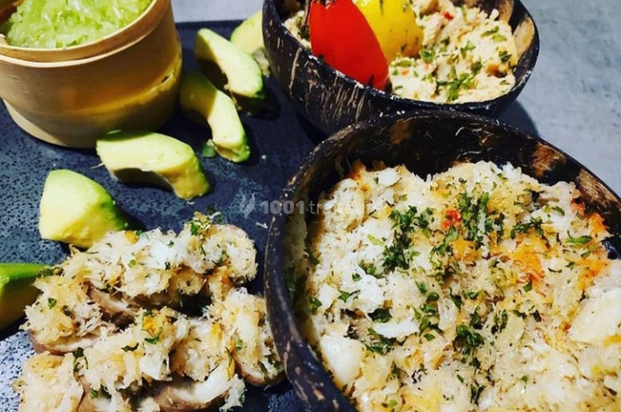 Assiette composée de rillettes de poisson servies dans des coques de noix de coco, accompagnées d'avocat et de crudités.