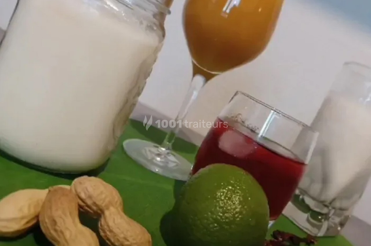 Boissons variées sur une table avec cacahuètes, citron vert et fleurs d'hibiscus en décoration.