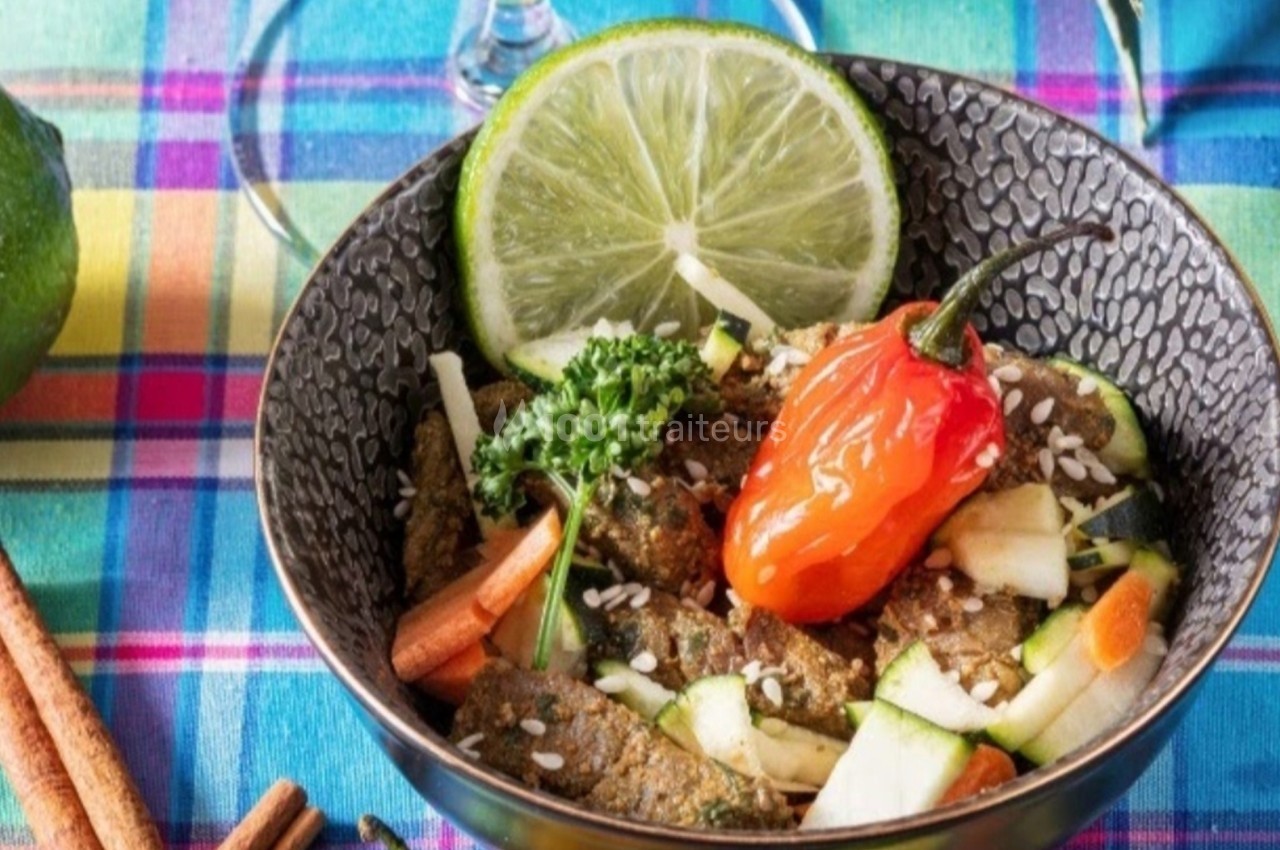 Bol de légumes frais avec citron vert, piment rouge, graines et herbes, sur une nappe colorée à carreaux.
