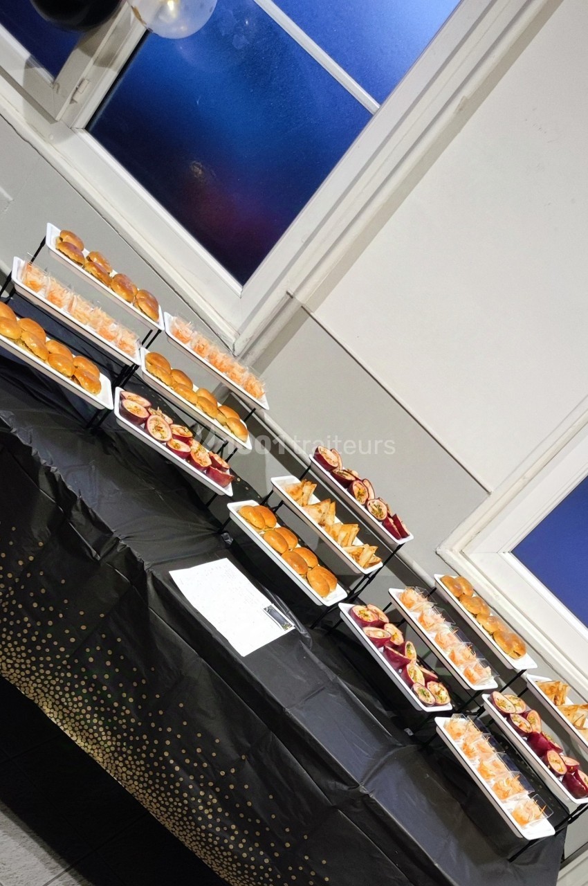Table garnie de plateaux de mini-sandwichs et amuse-bouches disposés sur une nappe noire décorée de motifs dorés.