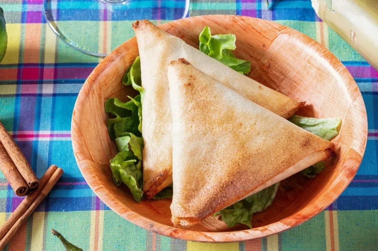 Deux samoussas dorés sur un lit de salade dans une assiette en bois, posée sur une nappe colorée.