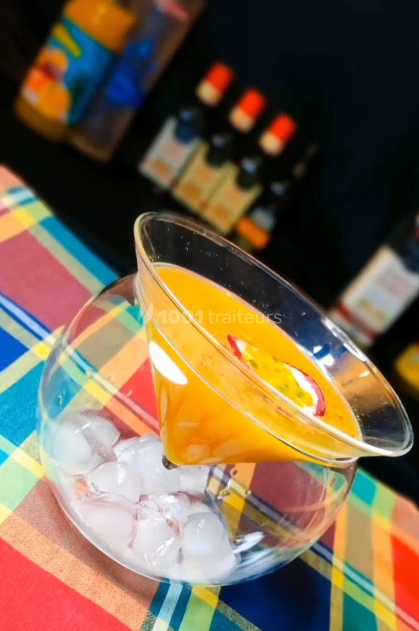 Cocktail orange servi dans un verre conique posé sur un récipient rempli de glaçons, avec une tranche de fruit en garniture.