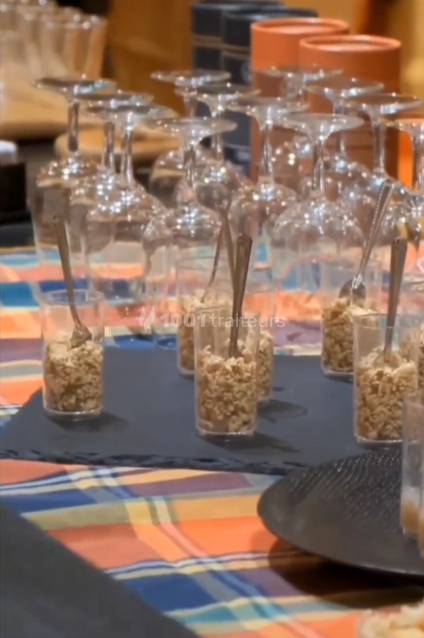 Verres à pied retournés et verrines de céréales avec cuillères, disposés sur une nappe colorée.