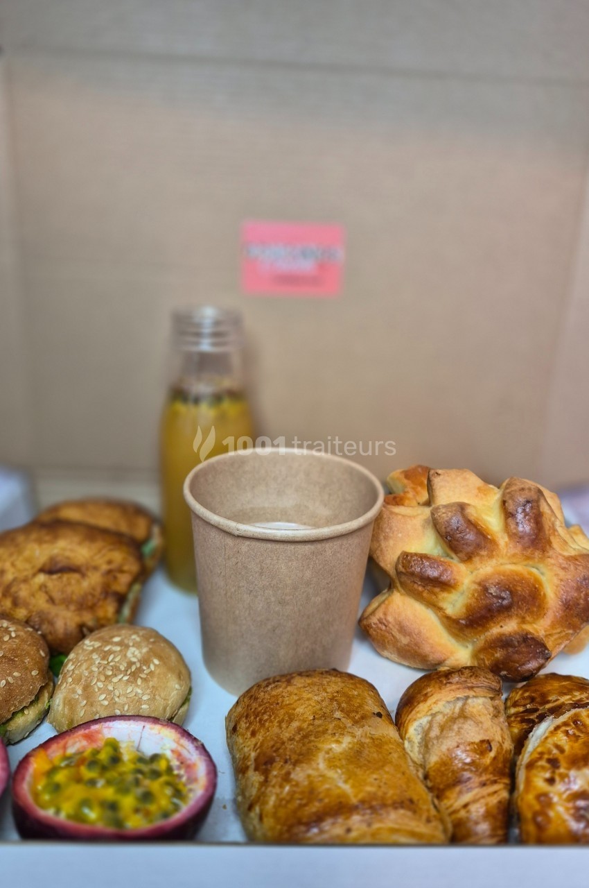 Plateau de viennoiseries, petits pains garnis, fruits de la passion, jus d'orange et boisson chaude dans un gobelet.