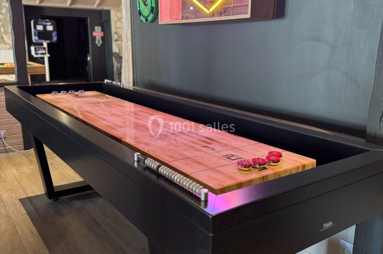Table de shuffleboard en bois avec des pions, située dans une pièce décorée d'une enseigne lumineuse ’Las Vegas’.