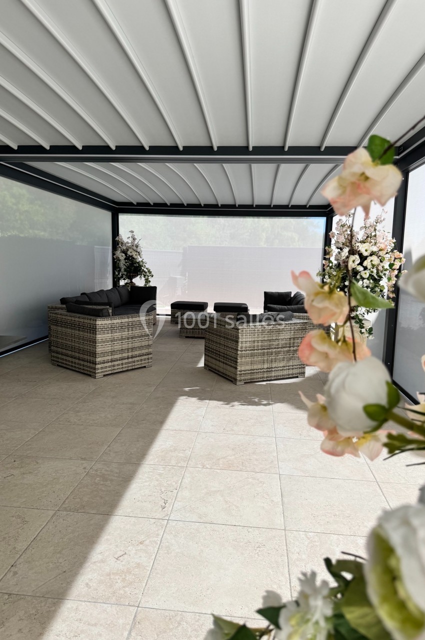 Salon de jardin avec mobilier en rotin sous une pergola moderne, entouré de fleurs et baigné de lumière naturelle.