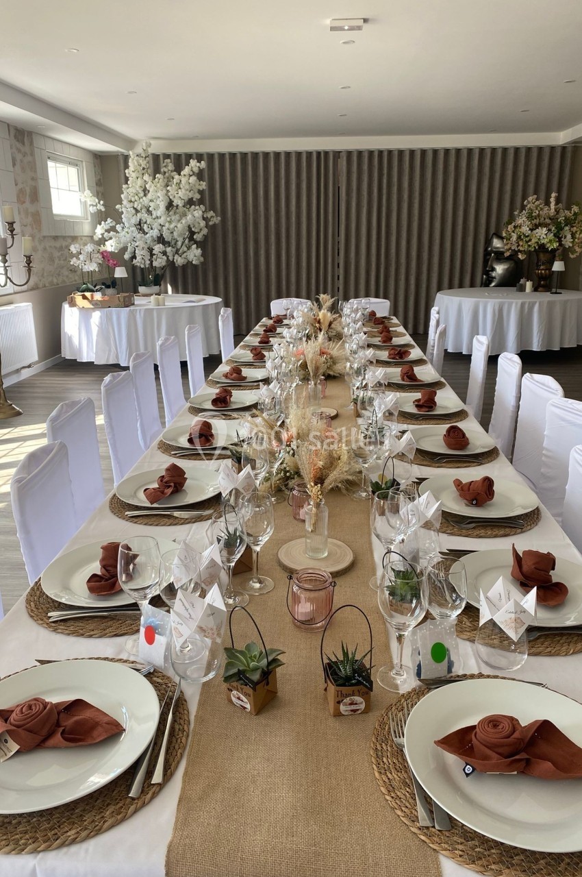 Grande table décorée pour un repas festif, avec nappes en toile de jute, serviettes pliées et centres de table fleuris.