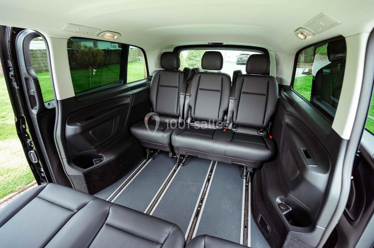 Intérieur d'un véhicule spacieux avec trois rangées de sièges noirs en cuir et un espace dégagé au sol.