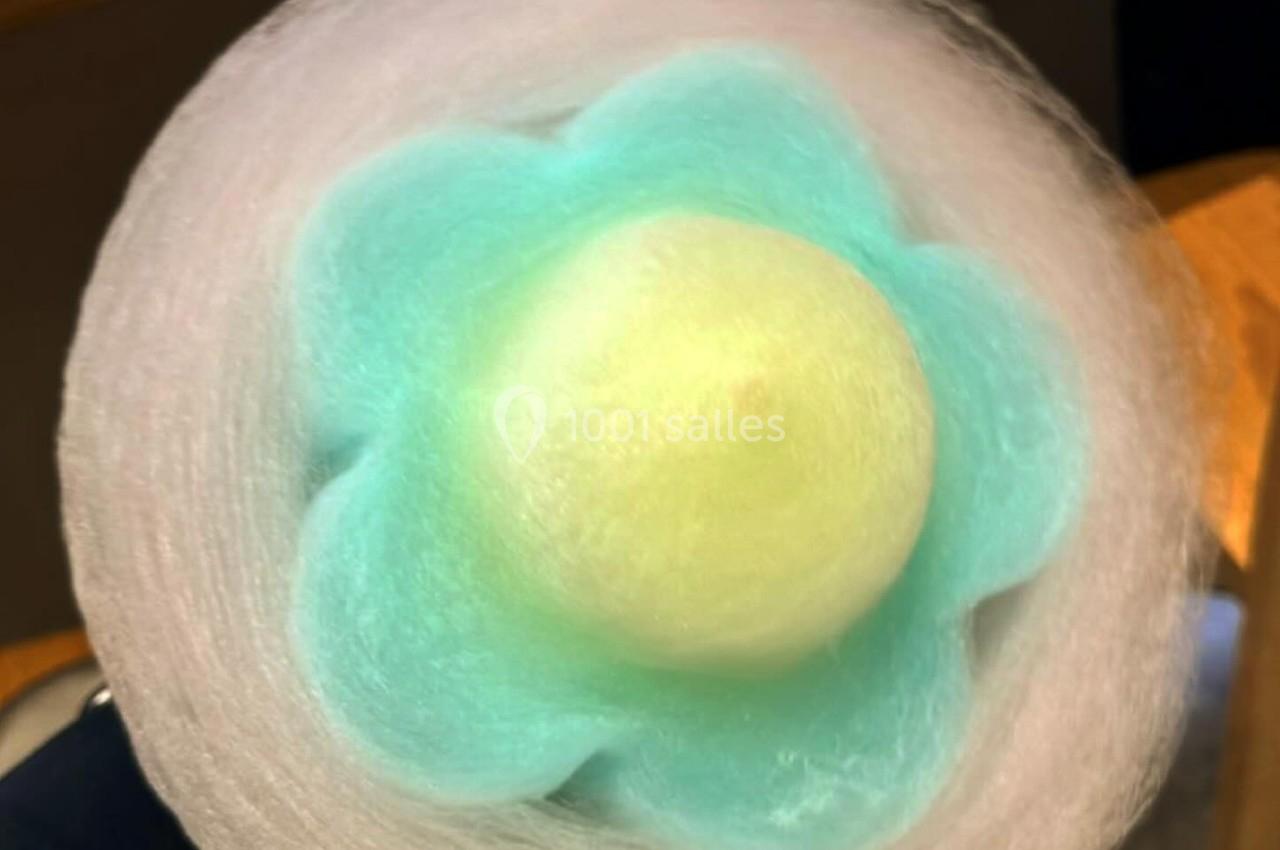 Barbe à papa en forme de fleur avec des couleurs pastel bleu, vert et blanc, posée sur un fond de table en bois.