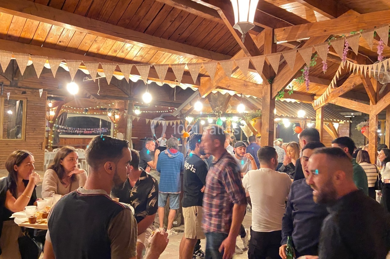 Des personnes discutent et mangent dans un espace en bois décoré de guirlandes et éclairé par des lampes suspendues.