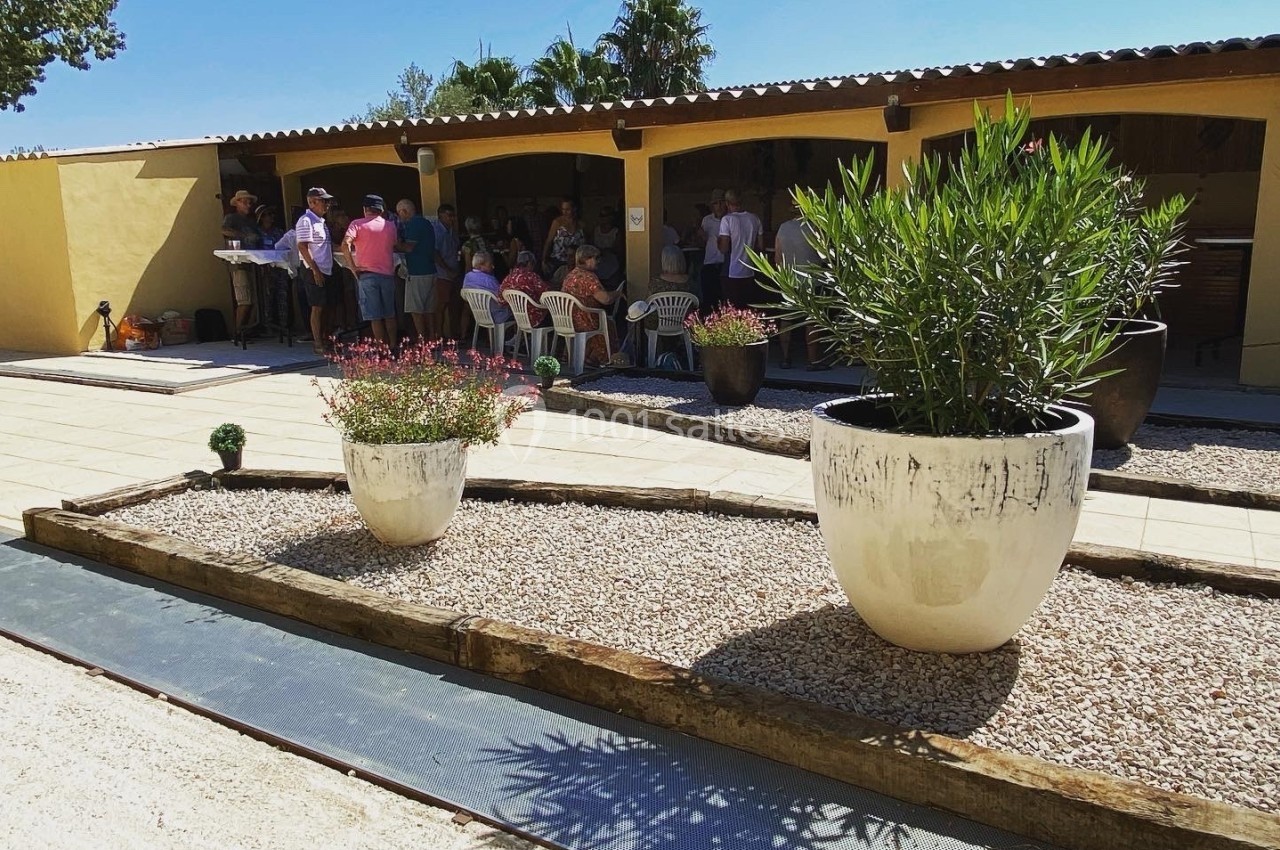 Des pots de fleurs blancs sur une terrasse en gravier devant un bâtiment avec des personnes rassemblées à l'ombre.