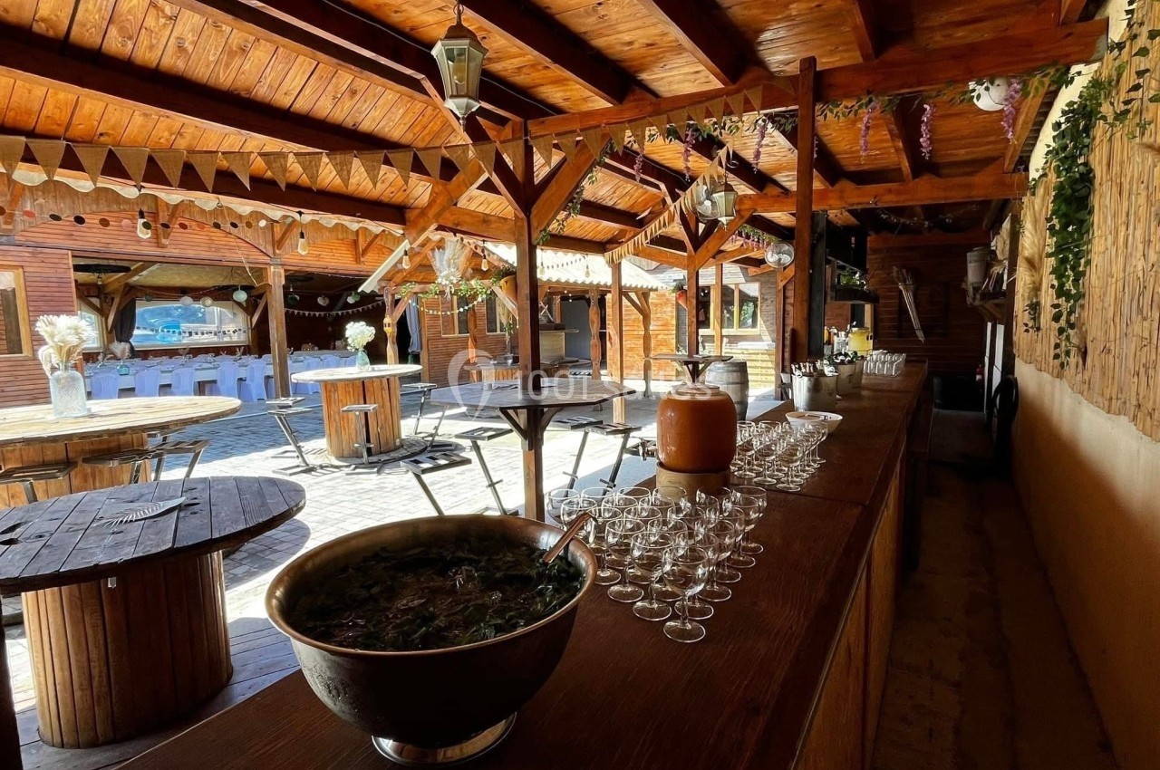 Salle en bois avec tables rondes, bar garni de verres et d'une grande coupe, décorée pour un événement festif.