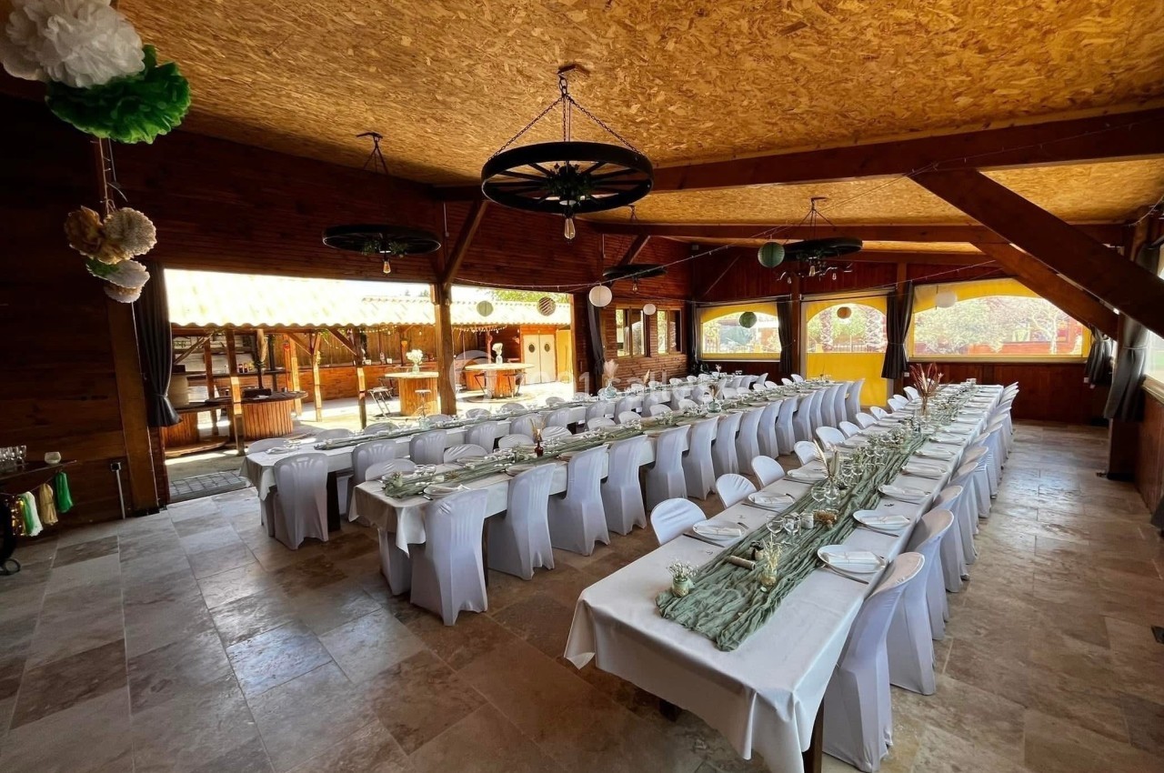 Salle décorée pour un banquet avec de longues tables dressées, nappes blanches et décoration champêtre.