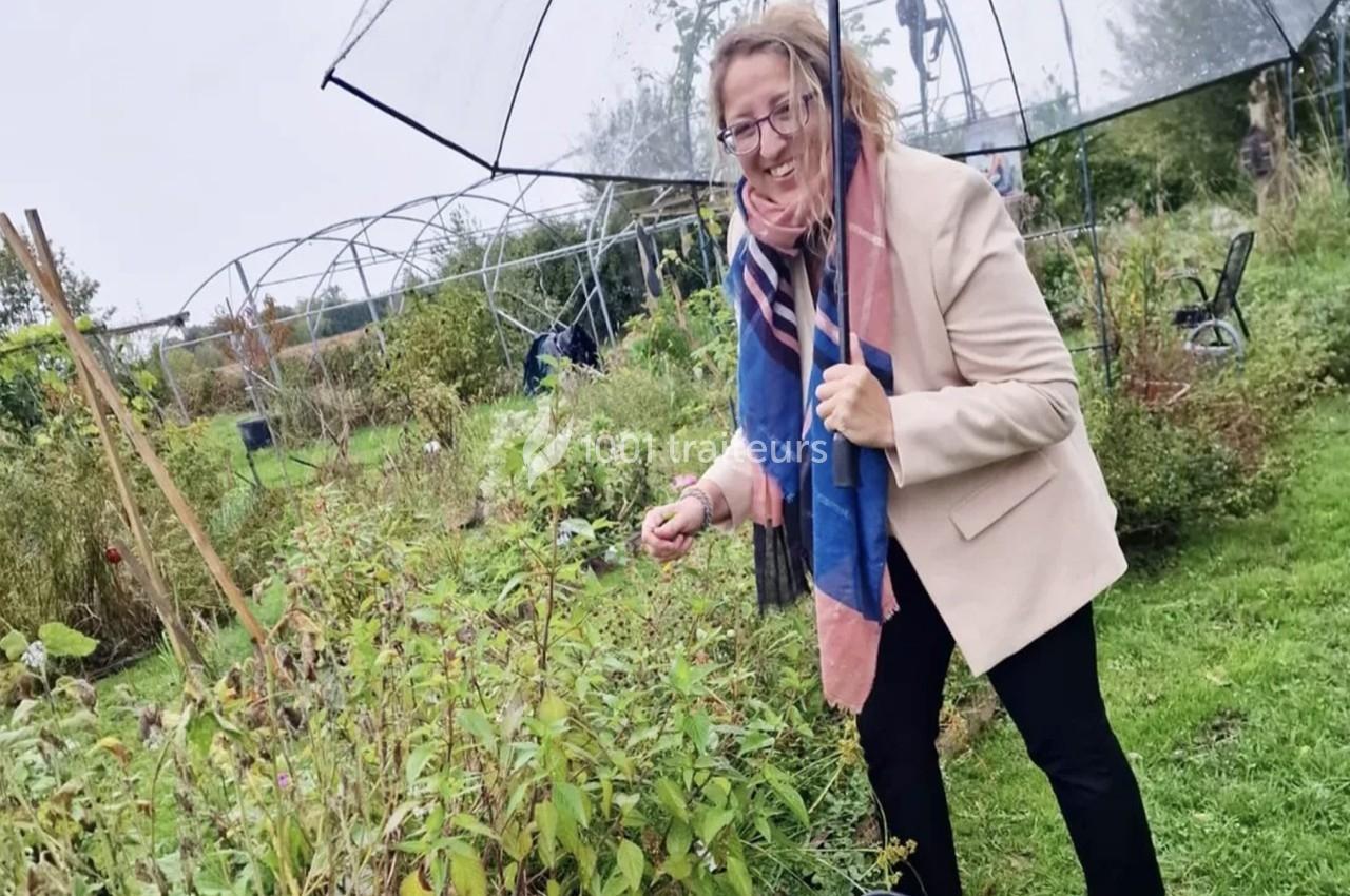 Femme souriante cueillant des baies dans un jardin sous un parapluie par temps nuageux.