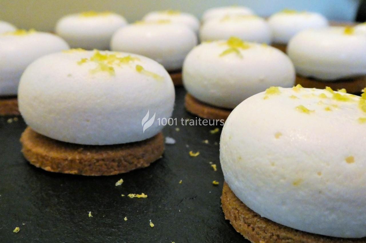 Desserts individuels ronds avec mousse blanche sur un biscuit, décorés de zestes de citron, disposés sur une surface noire.