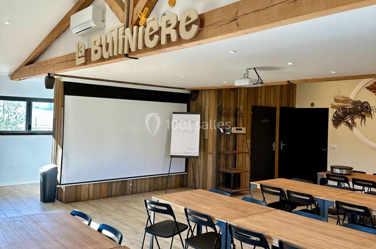 Salle équipée de tables, chaises, écran de projection et tableau blanc, décorée sur le thème des abeilles.