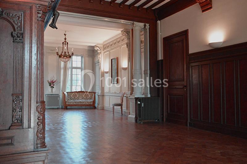 Salle élégante avec parquet en bois, canapé ancien, lustre, moulures et grandes fenêtres laissant entrer la lumière.