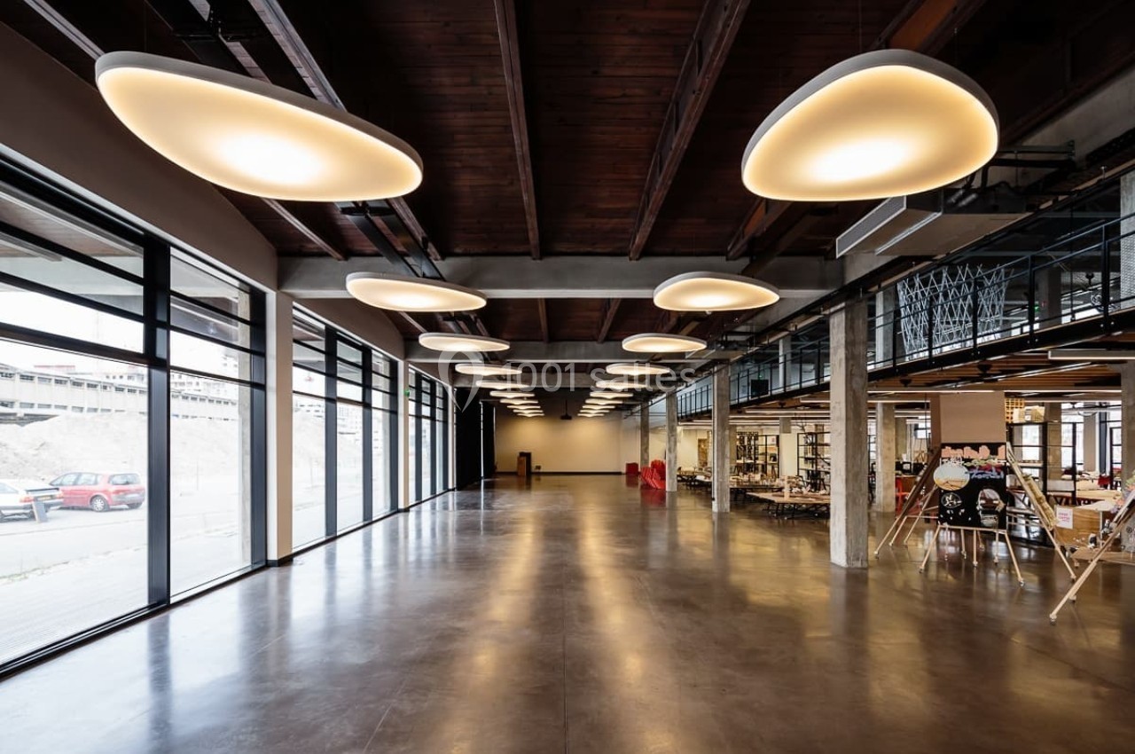 Salle spacieuse avec plafond en bois, luminaires modernes suspendus et grandes baies vitrées donnant sur l'extérieur.