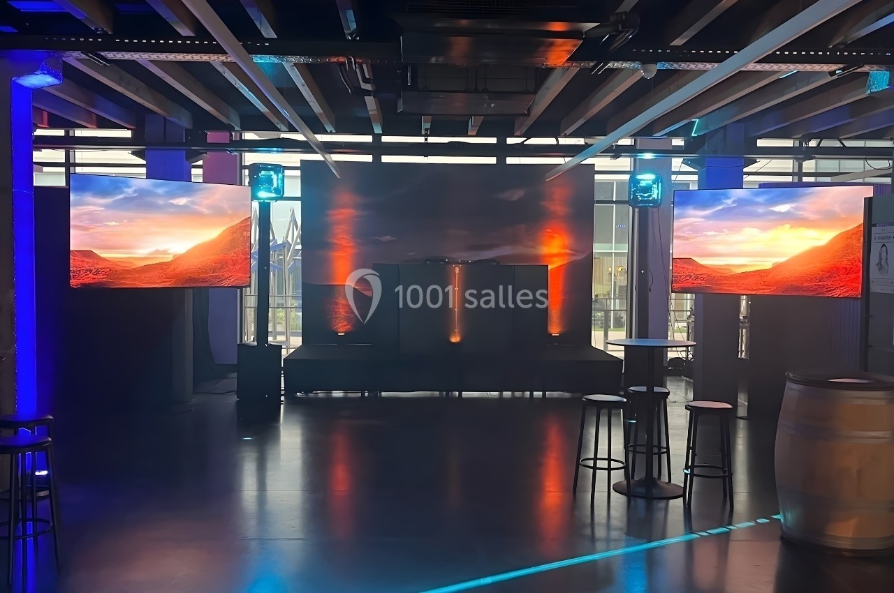 Salle sombre avec deux écrans affichant un paysage désertique, éclairages colorés et mobilier minimaliste.