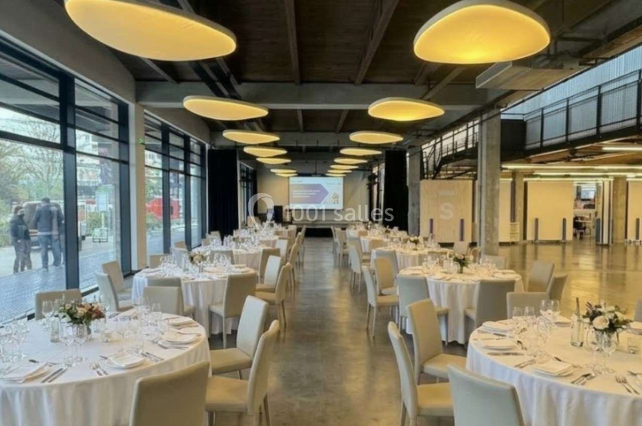 Salle de réception moderne avec tables rondes dressées, grandes baies vitrées et éclairage suspendu.