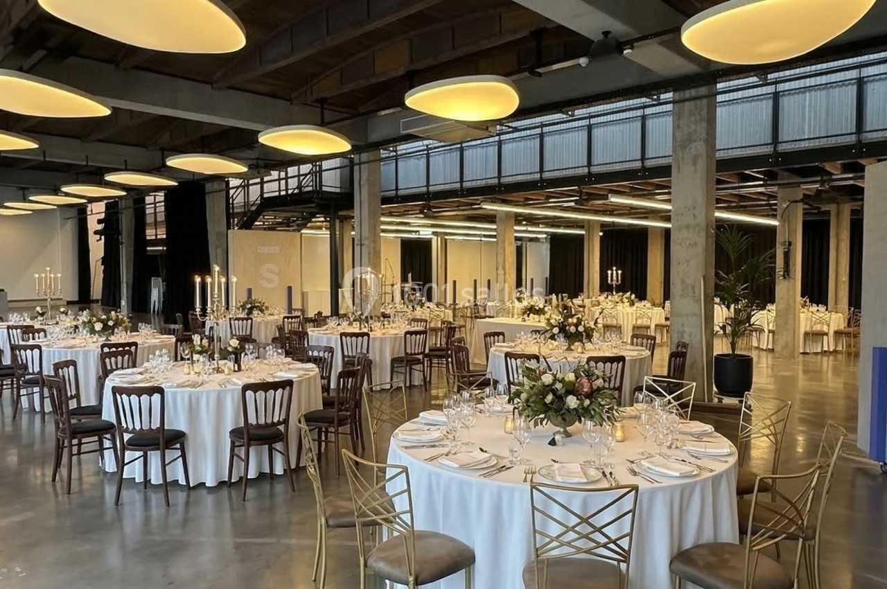 Salle de réception élégante avec tables rondes dressées, nappes blanches, chandeliers et éclairage suspendu moderne.