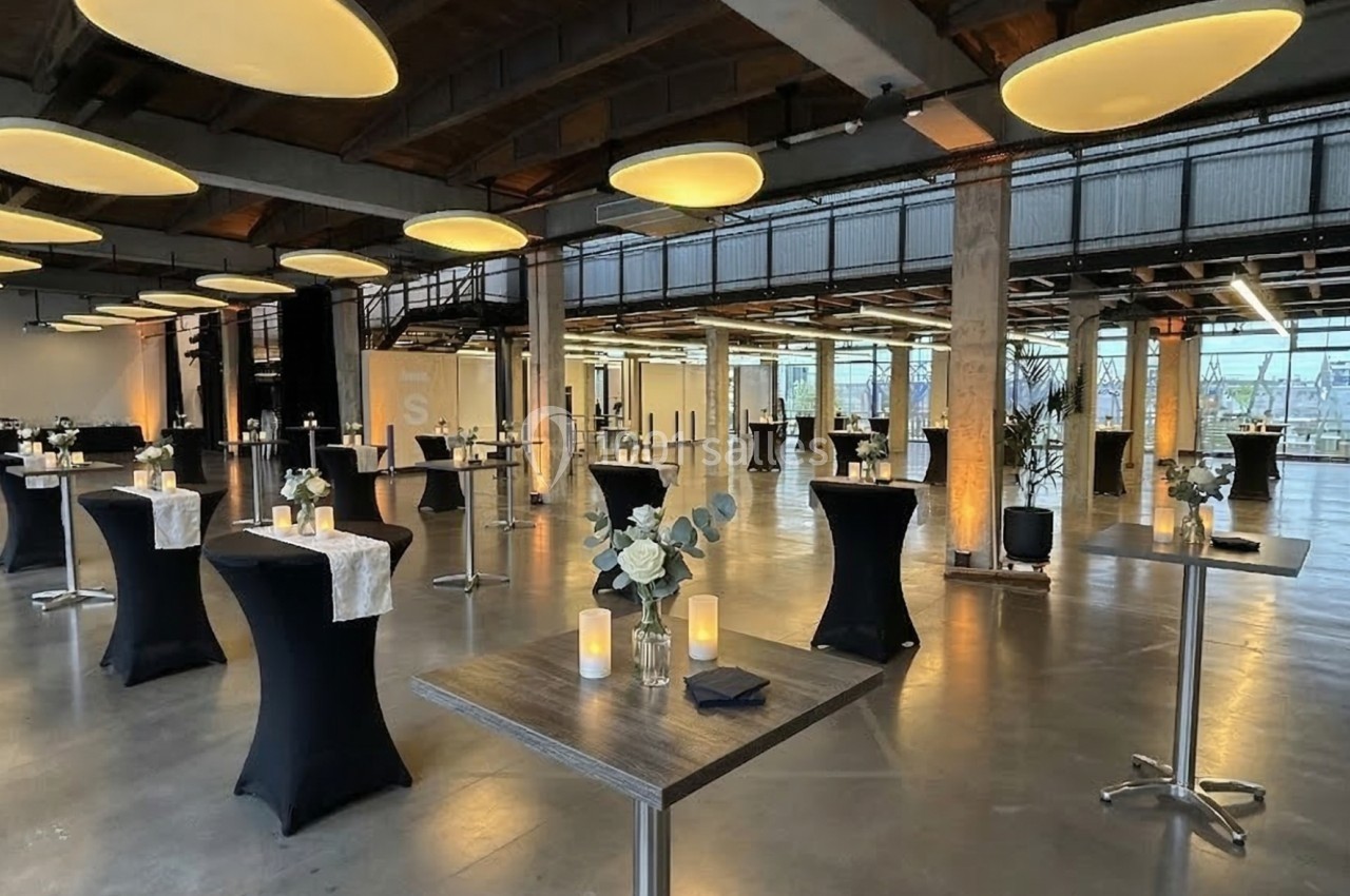 Salle moderne aménagée pour un événement, avec tables hautes décorées, bougies et éclairage chaleureux.