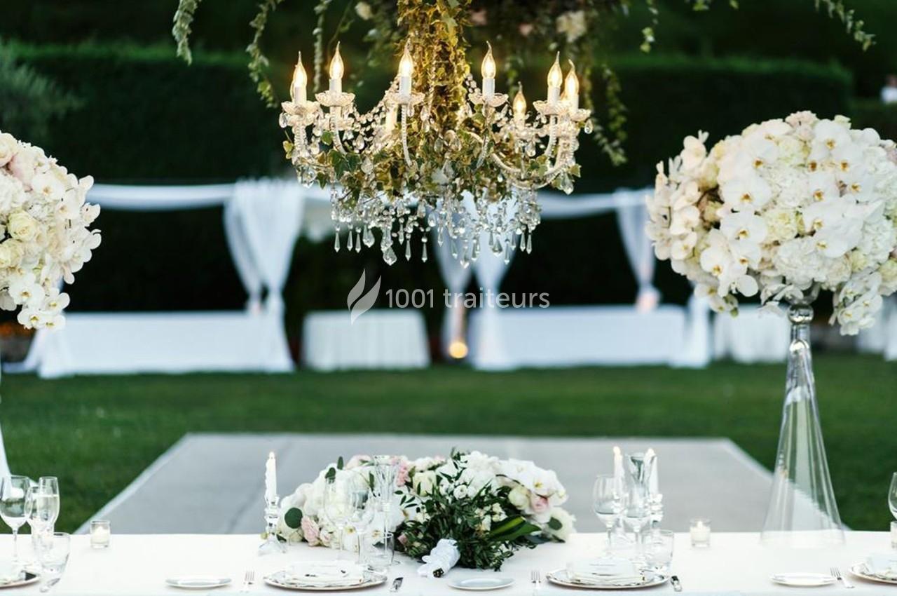Table décorée pour un événement en plein air avec chandelier suspendu, fleurs blanches et nappes élégantes.