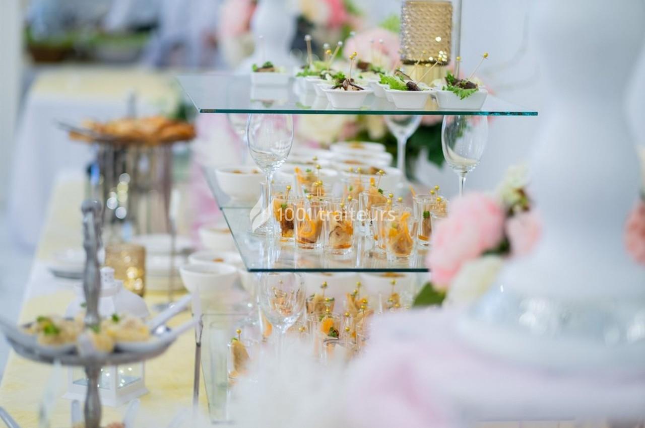 Buffet élégant avec verrines, plats variés et décorations florales sur une table en verre.
