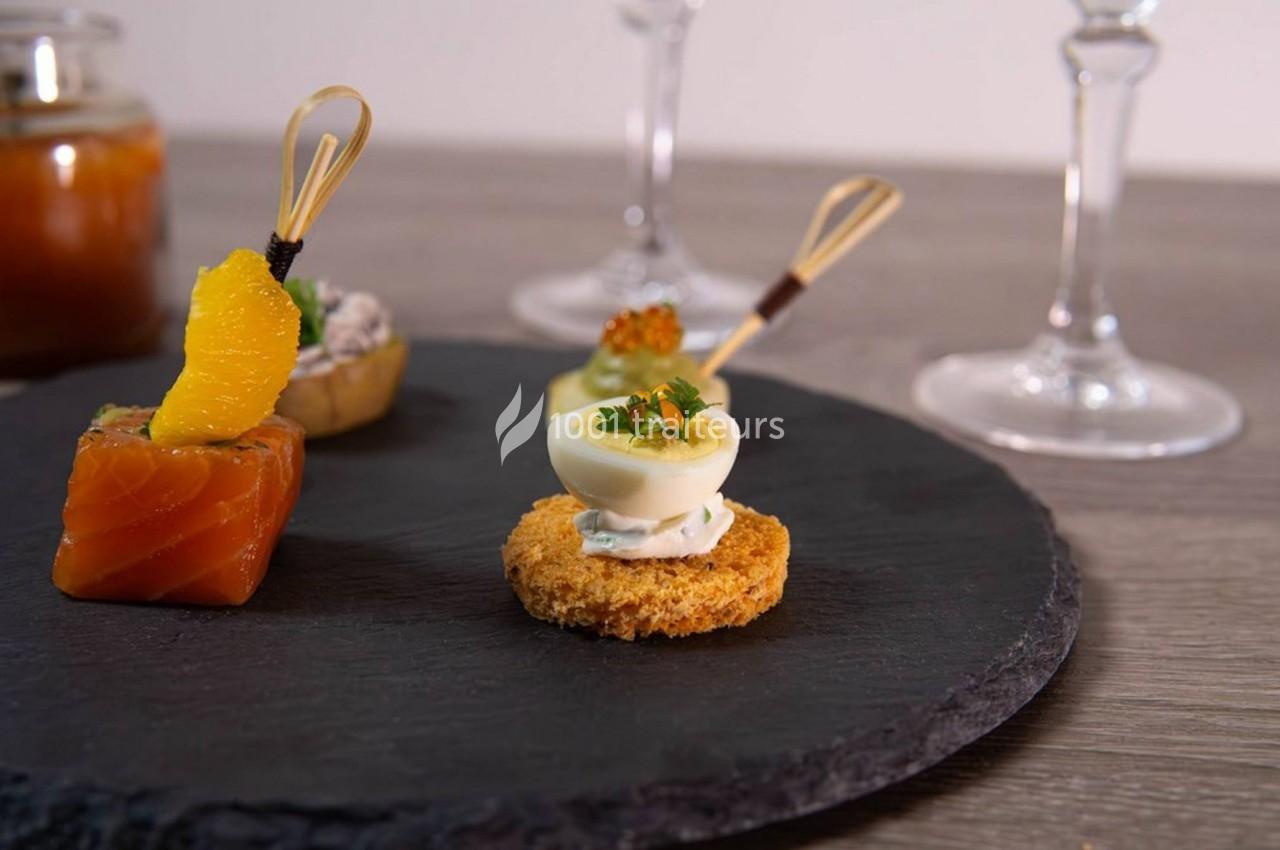 Assortiment de bouchées apéritives sur une ardoise, comprenant saumon, œuf farci et garnitures variées.