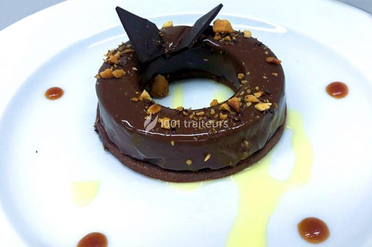 Dessert en forme d'anneau avec glaçage au chocolat, éclats de noisettes, décoration en chocolat et sauce autour.
