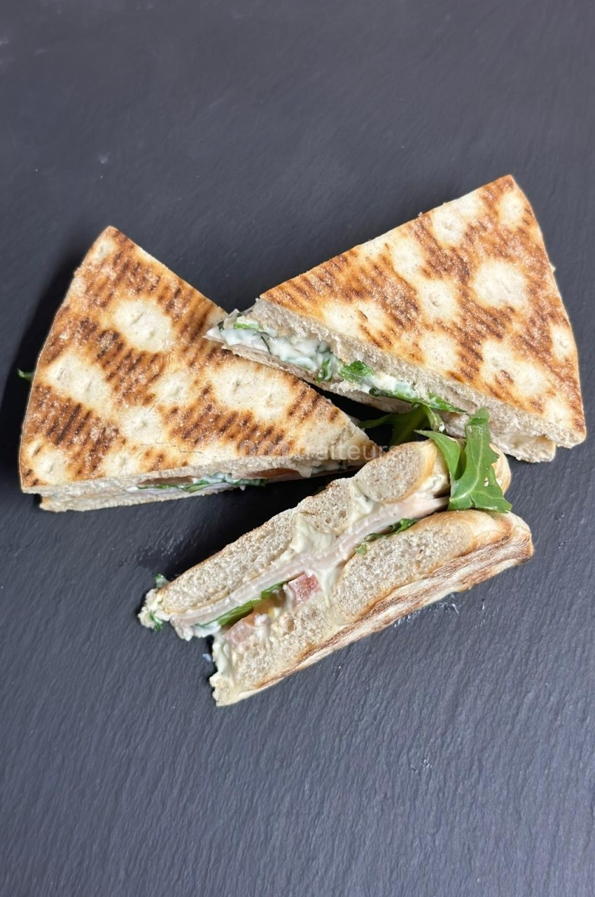 Triangles de sandwichs grillés garnis de roquette, fromage et autres ingrédients, présentés sur une surface sombre.