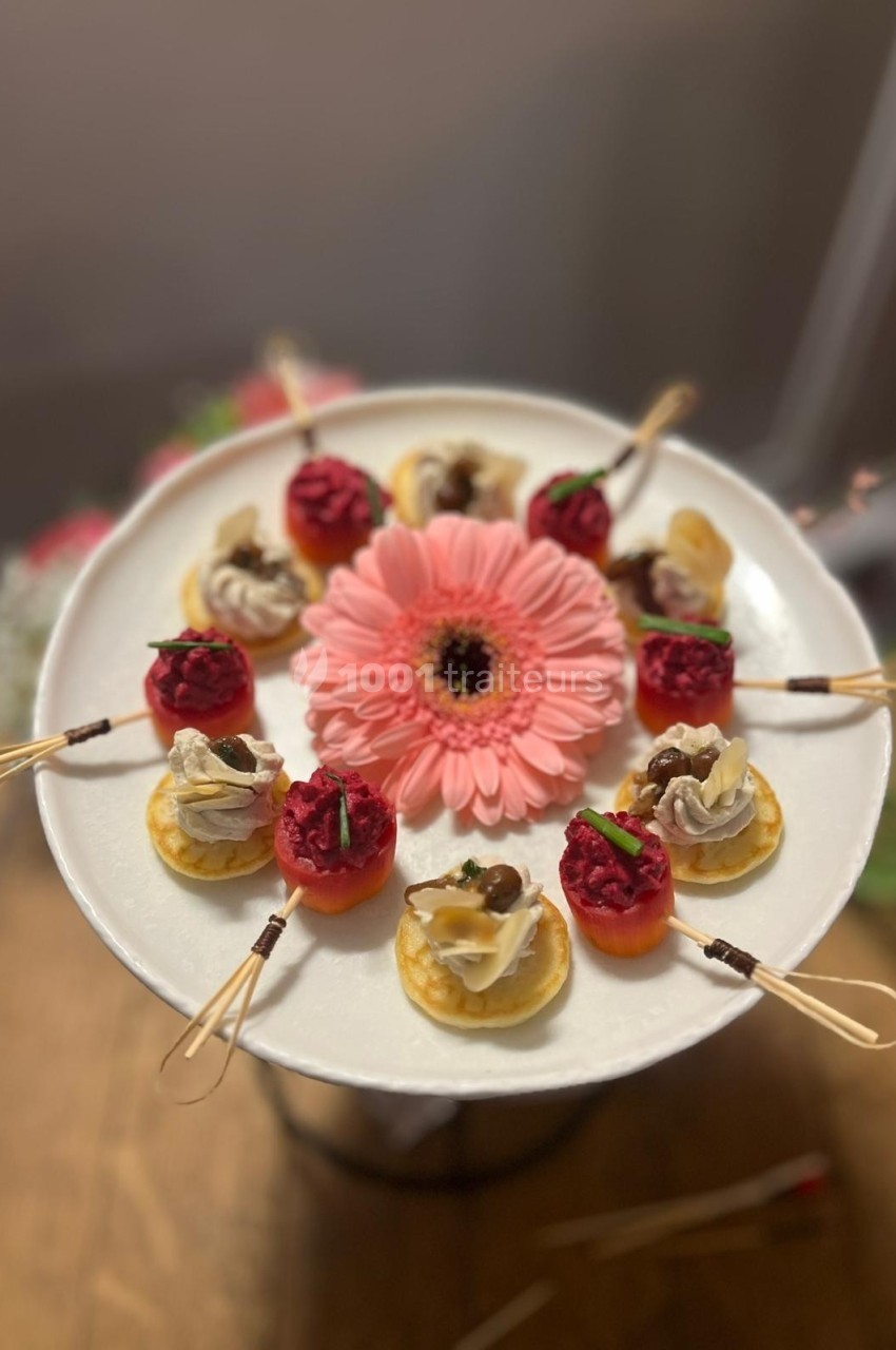 Assortiment de bouchées apéritives disposées sur un plateau blanc avec une fleur rose en son centre.