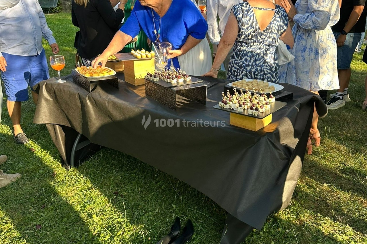 Des personnes se servent à un buffet en plein air, avec des amuse-bouches disposés sur une table recouverte d'une nappe…